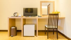 A hotel room with a wooden desk, a television, a small refrigerator, a trash bin, a chair, and a mirror. - My Living Place Chaweng Beach (Koh Samui)