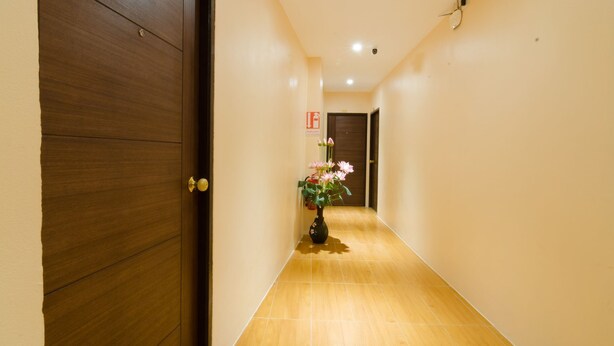 A hallway with a wooden door on the left, a tiled floor, and a vase with flowers in the center. - My Living Place Chaweng Beach (Koh Samui)