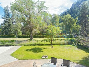 Un patio con mesa y sillas, rodeado de césped cuidado y árboles.