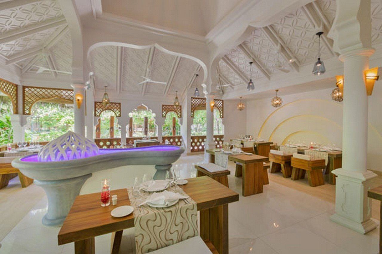 A restaurant with a central fountain, wooden tables, and a white ceiling with intricate patterns.
