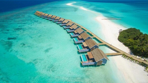 An overwater bungalow resort with a long pier connecting to the beach, clear turquoise waters, and lush greenery. - Niva Kuramathi Maldives (Kuramathi Island)