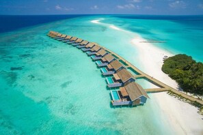 An overwater bungalow resort with a long pier connecting to the beach, clear turquoise waters, and lush greenery. - Niva Kuramathi Maldives (Kuramathi Island)