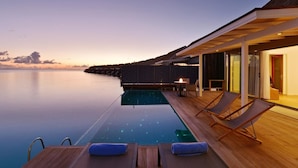 An infinity pool with lounge chairs and a table, overlooking a calm sea and overwater bungalows. - Niva Kuramathi Maldives (Kuramathi Island)