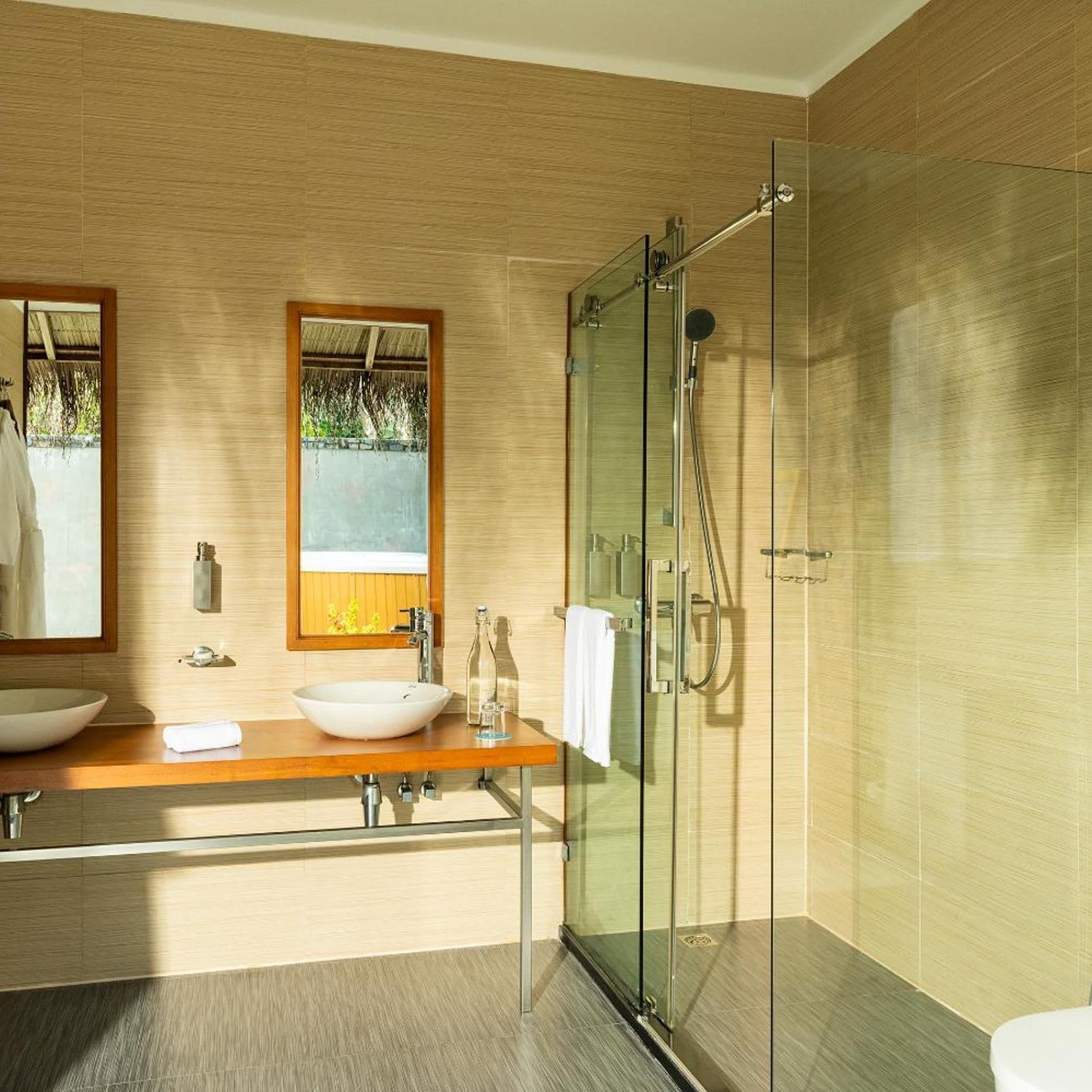 A modern bathroom with a glass-enclosed shower, a wooden vanity with a bowl sink, and a large mirror.