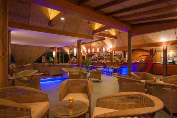 A lounge area with wicker furniture, a bar, and a pool with blue lighting.