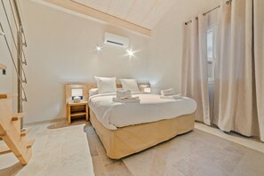 A hotel room with a large bed, a bedside table, a nightstand, a wooden chair, a window with curtains, and an air conditioning unit. - Villa-Superior-Ensuite with Shower-Pool view (Saint-Maurice-d’Ardèche)
