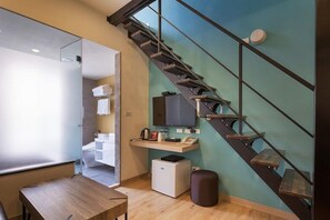 Ein modernes Hotelzimmer mit einem Holztisch, einem kleinen weißen Kühlschrank, einer integrierten Bank und einem Glaskabinentuchbereich.