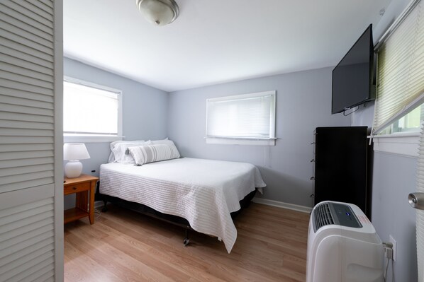 A bedroom with a bed, bedside table, lamp, window blinds, and a TV mounted on the wall. - A Horse Racing Enthusiast's Delight / SPAC (Saratoga Springs)