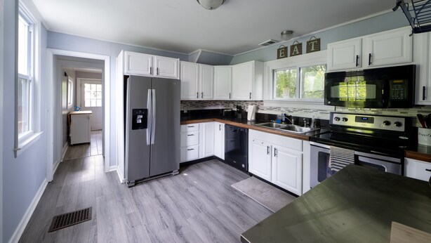 Una cocina moderna con armarios blancos, un refrigerador de acero inoxidable, un microondas negro y una encimera de madera.