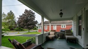 Un porche cubierto con mobiliario exterior, vista a una calle residencial y una casa al fondo.