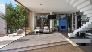 A modern living room with a sofa, coffee table, and TV. There is a fireplace and a staircase with a view of the outside. - Almond Villa (Rhodes)