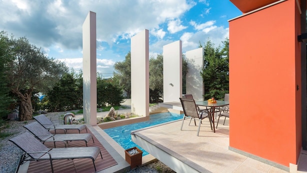 A modern outdoor pool area with lounge chairs, a table with fruit, and a clear sky. - Almond Villa (Rhodes)