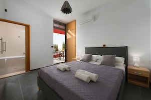 Un dormitorio moderno con una cama grande, una mesita de noche, un ventanal y un equipo de aire acondicionado.