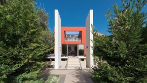 A modern house with a red facade, a glass entrance, and a pathway leading to the front door. - Almond Villa (Rhodes)