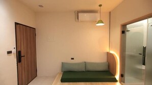Ein Zimmer mit Holztür, einem grünen Sofa, einer Deckenleuchte und einer Klimaanlage.
