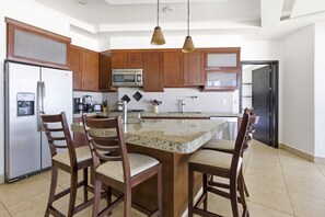 Una cocina moderna con encimeras de granito, armarios de madera, electrodomésticos de acero inoxidable y una isla central con taburetes de bar.