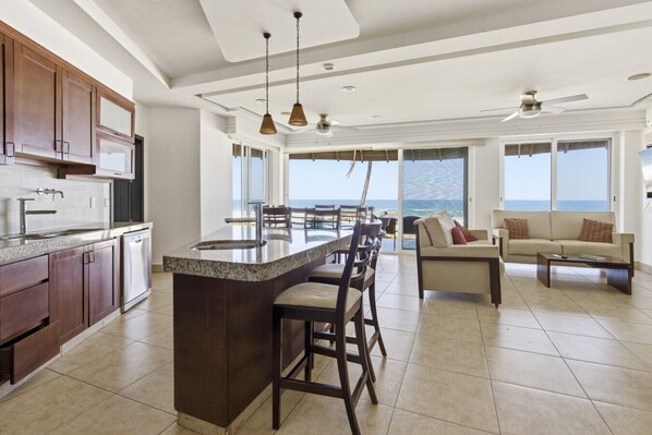 Una cocina moderna con una isla central, un área de comedor con vistas y una sala de estar con sofá y mesa de centro.