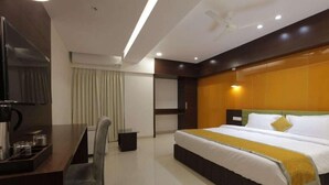 A hotel room with a bed, a desk with a chair, a television, and a window with curtains. - Hotel The Lotus Park (Ahmedabad)