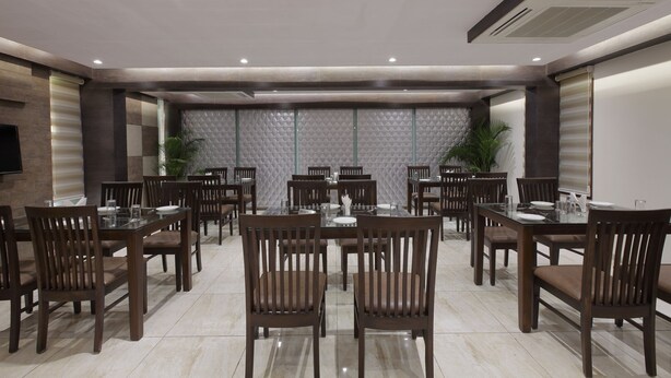 A spacious dining area with multiple tables and chairs, a modern ceiling design, and a large screen on the wall. - Hotel The Lotus Park (Ahmedabad)