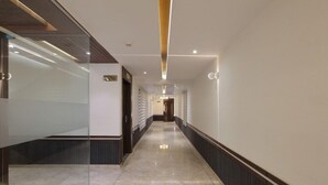 A modern hotel corridor with glass walls, a polished marble floor, and recessed lighting. - Hotel The Lotus Park (Ahmedabad)
