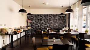 A modern restaurant with a central bar area, multiple dining tables, and black pendant lighting. - Hotel Shato (Prague)