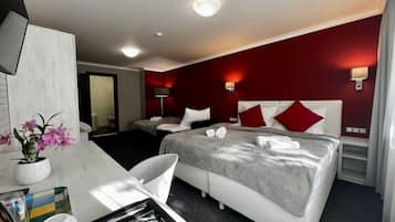 A hotel room with a bed, bedside tables, a desk with a chair, a vase with flowers, and a tray with items.