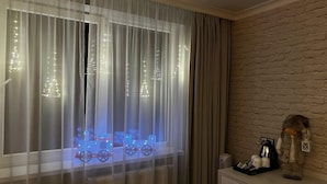 A room with a window featuring sheer curtains and Christmas lights forming tree shapes. - Hotel Shato (Prague)