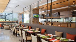 A modern restaurant with a long dining area, high ceilings, and a view of the outdoors. - Renaissance Ahmedabad Hotel (Ahmedabad)