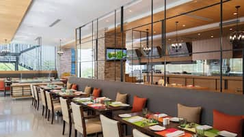 A modern restaurant with a long dining area, high ceilings, and a view of the outdoors.