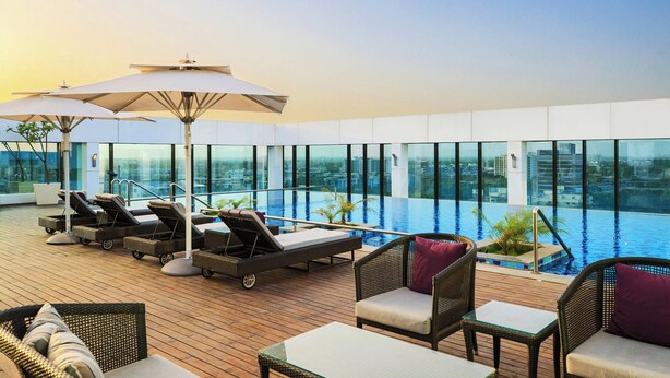 A rooftop infinity pool with lounge chairs and umbrellas, large windows, and a wooden deck. - Renaissance Ahmedabad Hotel (Ahmedabad)
