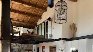 A spacious living area with a wooden ceiling, a dining table with chairs, a sofa, and a kitchen area in the background. - Le Pallier + extension (DIO-ET-VALQUIERES)