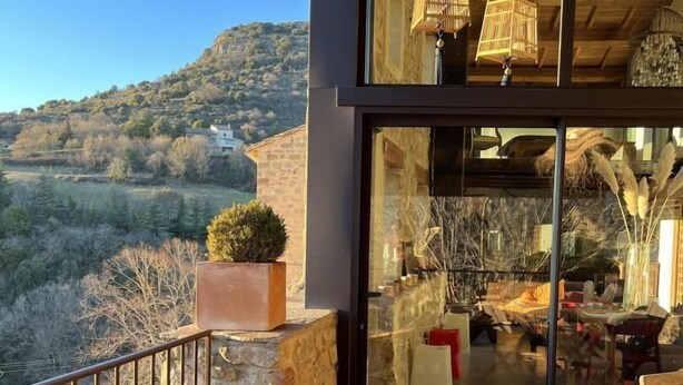A modern outdoor seating area with a wicker chair and a glass wall overlooking a scenic landscape. - Le Pallier + extension (DIO-ET-VALQUIERES)