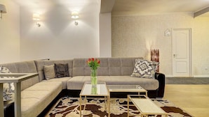 A modern living room with a grey sofa, two side tables, a vase with red flowers, patterned wallpaper, and a door in the background. - Inn Bairro Alto Bed & Breakfast (Lisbon)
