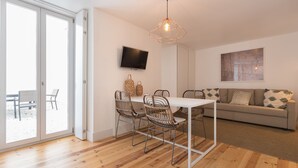 A modern living room with a dining area, a sofa, and a TV mounted on the wall. - Chiado Studios By Lu Holidays (Lisbon)