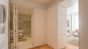 A modern, minimalist room with a wooden floor, a sliding door leading to a bathroom, and a small seating area with a chair and table. - Chiado Studios By Lu Holidays (Lisbon)