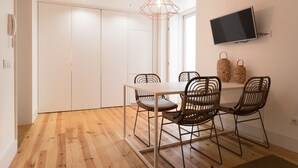 A dining area with a white table, wicker chairs, a hanging light fixture, and a mounted TV. - Chiado Studios By Lu Holidays (Lisbon)