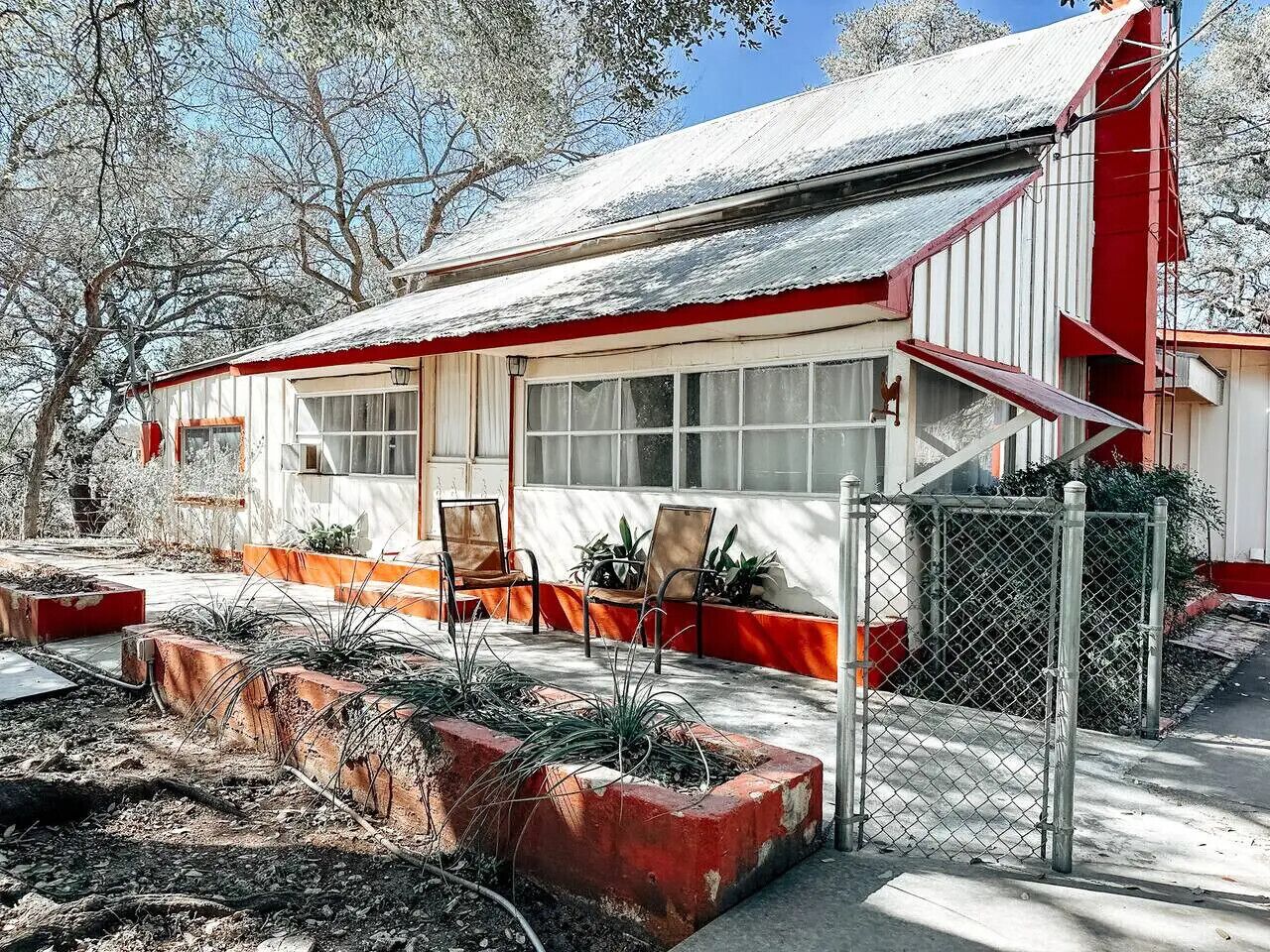 A single-story building with a red and white exterior, a covered porch with chairs, and a fenced garden area.