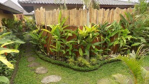A garden with a stone pathway, bamboo fence, and tropical plants. - Hideaway Villas Candy Ubud (Ubud)