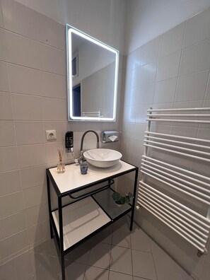 A modern bathroom with a white sink, a mirror with LED lighting, a towel rack, and a glass shelf. - Pension Hargita (Vienna)
