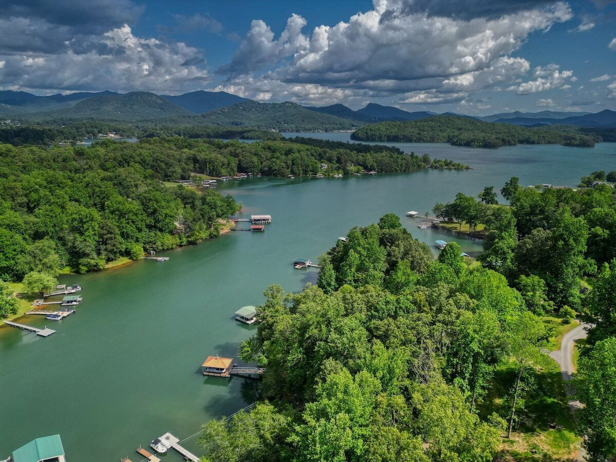Vista d'un llac amb barques amarrades a la riba, envoltada de vegetació abundant i muntanyes al fons.