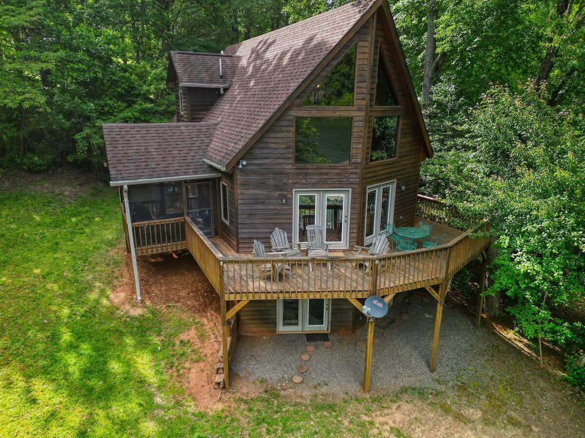 A wooden cabin with a deck, multiple windows, and a gravel driveway.