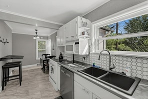 A modern kitchen with a large island, stainless steel appliances, and a view of greenery outside.