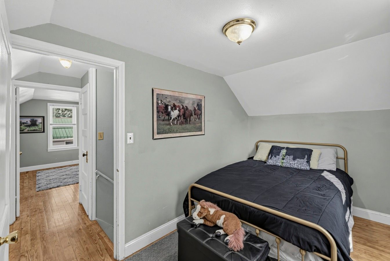 A bedroom with a bed, a ceiling light, a framed picture, and a door leading to another room.