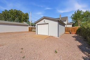 A single-story building with a garage, surrounded by a gravel driveway and a wooden fence.