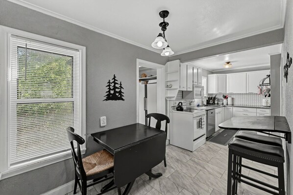 A modern kitchen with white cabinets, a black countertop, and a dining area with a black table and chairs. - Cozy Rapid City Home w/ Hot Tub & Patio (Rapid City)