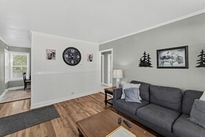 A living room with a grey sofa, a wooden coffee table, a clock, and framed pictures on the wall. - Cozy Rapid City Home w/ Hot Tub & Patio (Rapid City)