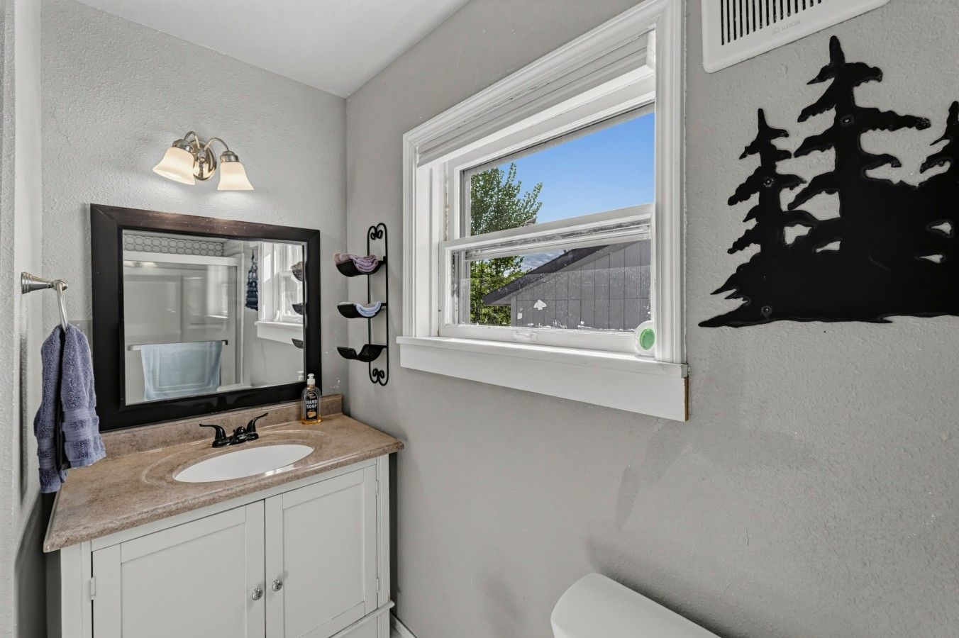 A bathroom with a sink, mirror, towel rack, window, and a wall decal.