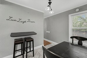 A dining area with a dark wooden table and two stools, a wall-mounted light fixture, and a window with blinds. - Cozy Rapid City Home w/ Hot Tub & Patio (Rapid City)