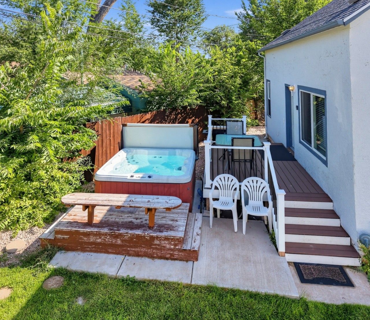 A backyard with a hot tub, a picnic table, and a deck with chairs.
