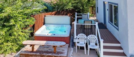 A backyard with a hot tub, a picnic table, and a deck with chairs.